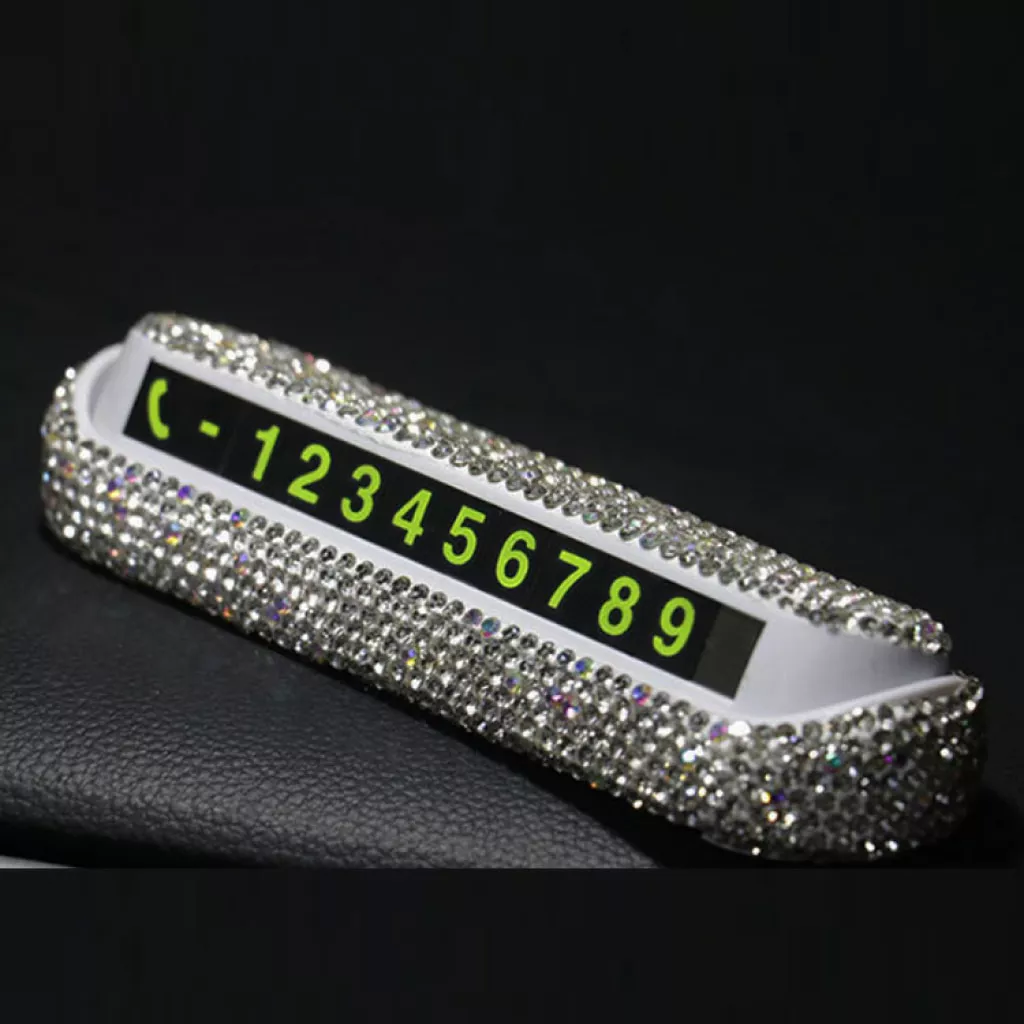 A sparkly, rhinestone-encrusted temporary parking phone number card is displayed on a dark surface. The card features a black panel with bright green numbers from 1 to 9 and a phone icon on the left side.