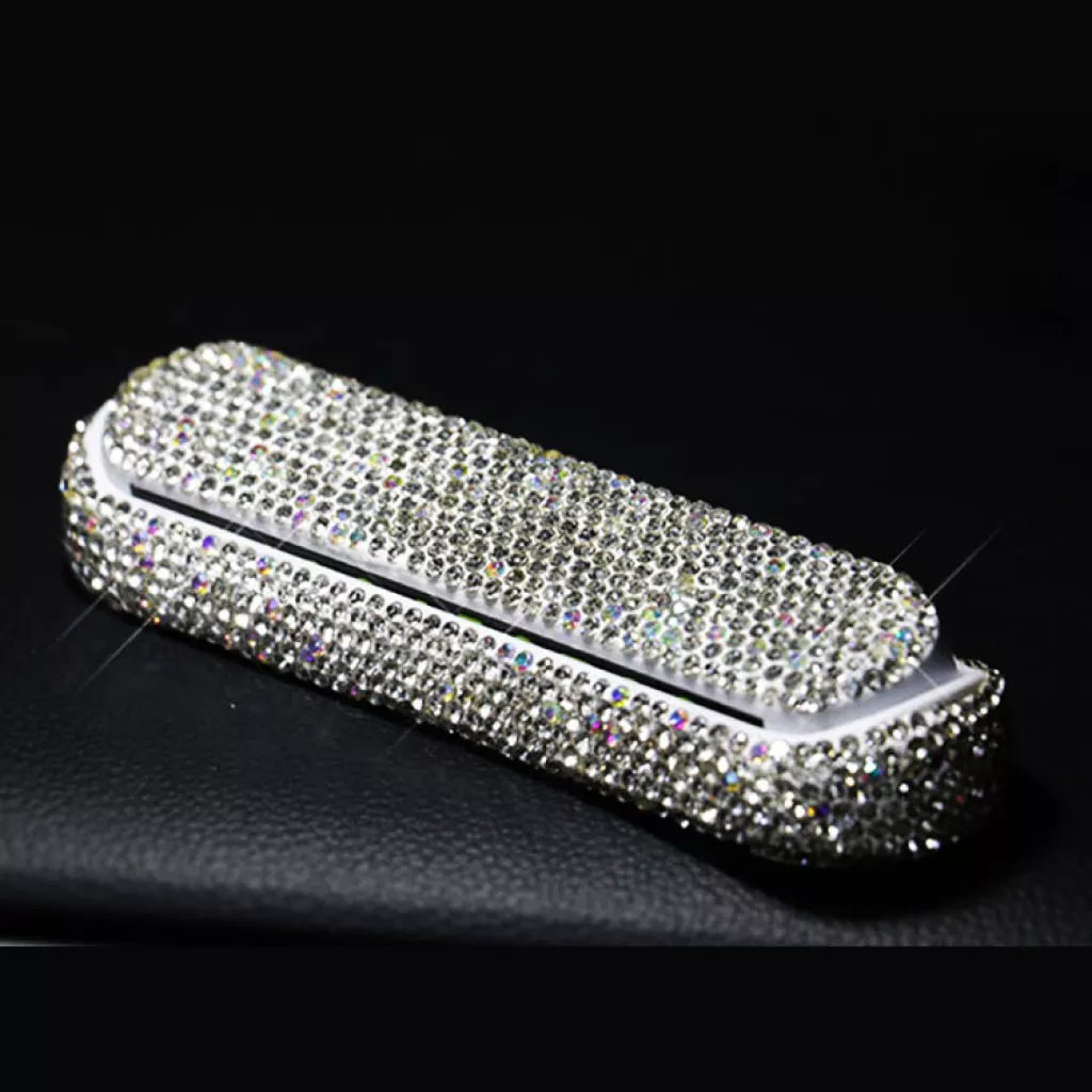 A compact, rectangular case is covered in sparkling rhinestones, reflecting light brightly on a black background.