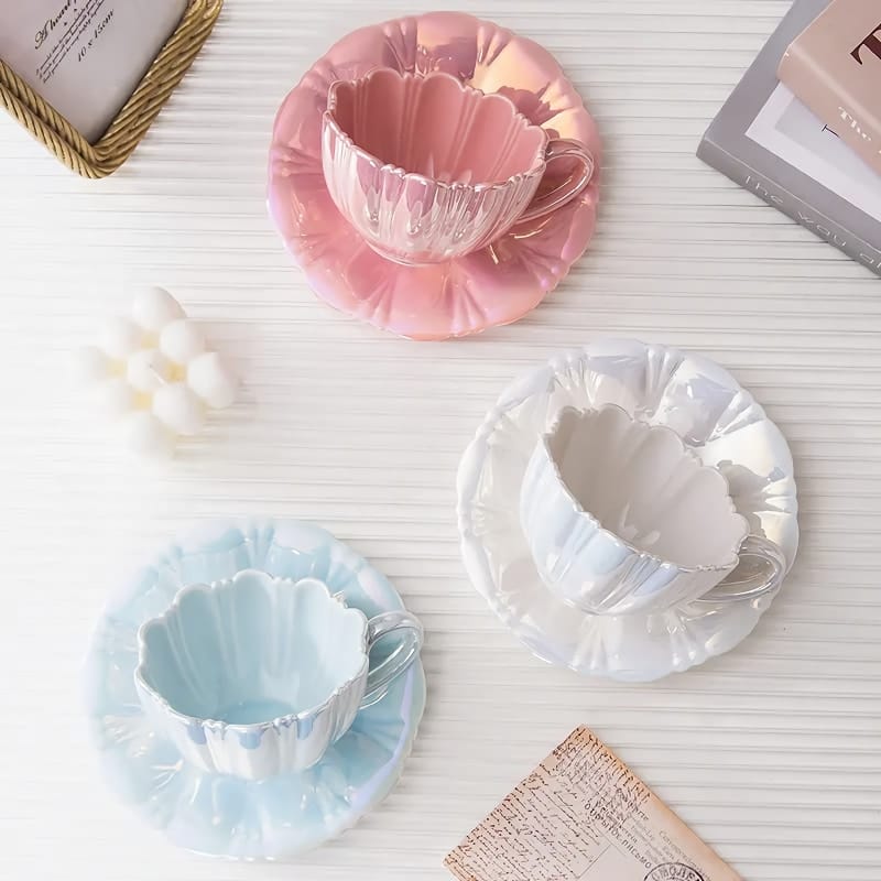 Three pastel teacup sets on a white surface: one pink, one blue, and one iridescent. Theres a cluster of white wax melts and a corner of a book in the top left corner.