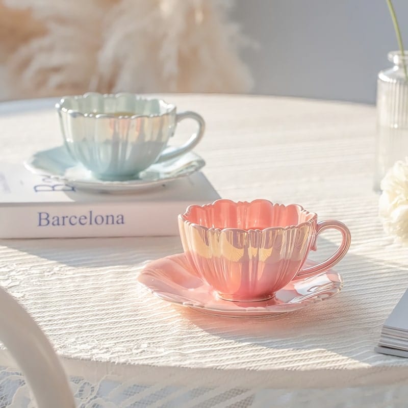 Two elegant teacups with saucers, one pink and one pale blue, sit on a lace-covered table. A book titled Barcelona is underneath the blue cup. Soft natural light creates a serene atmosphere.