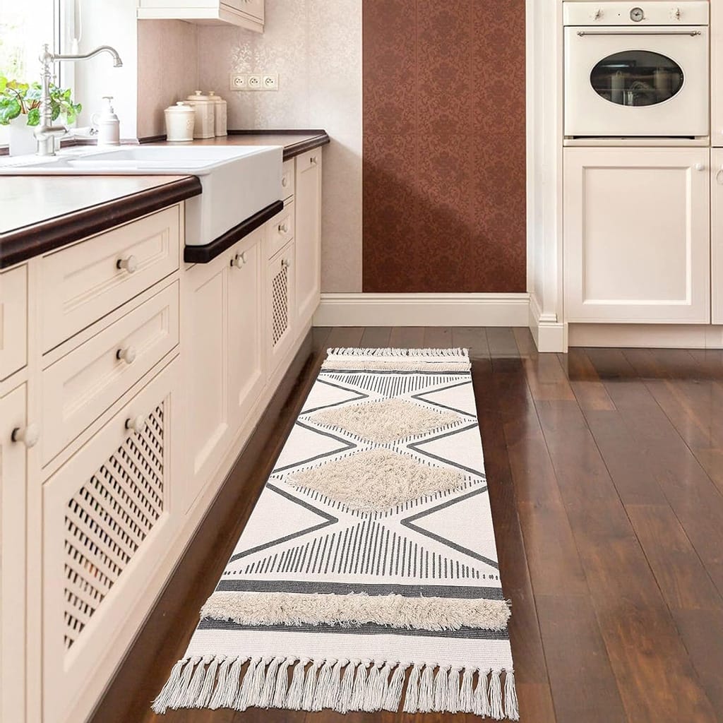 A narrow kitchen with white cabinetry and a wooden countertop. A patterned rug with geometric designs runs along the floor. An oven is built into the wall cabinetry, and a window provides natural light.