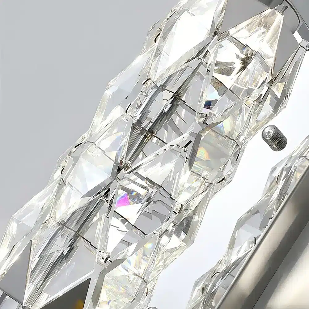 Close-up of a modern crystal chandelier with geometric, faceted glass elements reflecting light. The intricate pattern creates a sparkling effect, casting subtle rainbow hues.