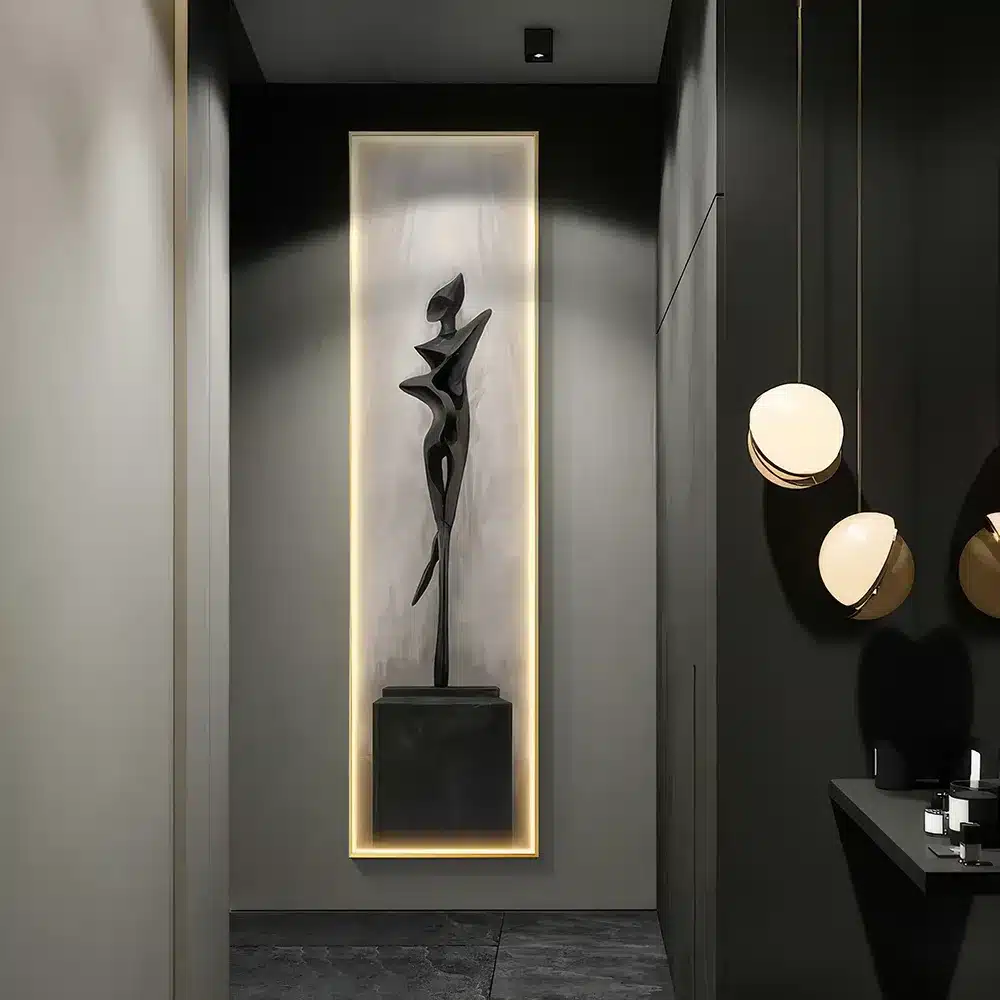 A sleek, modern hallway with a tall, abstract black sculpture displayed on a pedestal, illuminated by soft lighting. Minimalist décor includes round pendant lights on the right, creating a contemporary and elegant atmosphere.