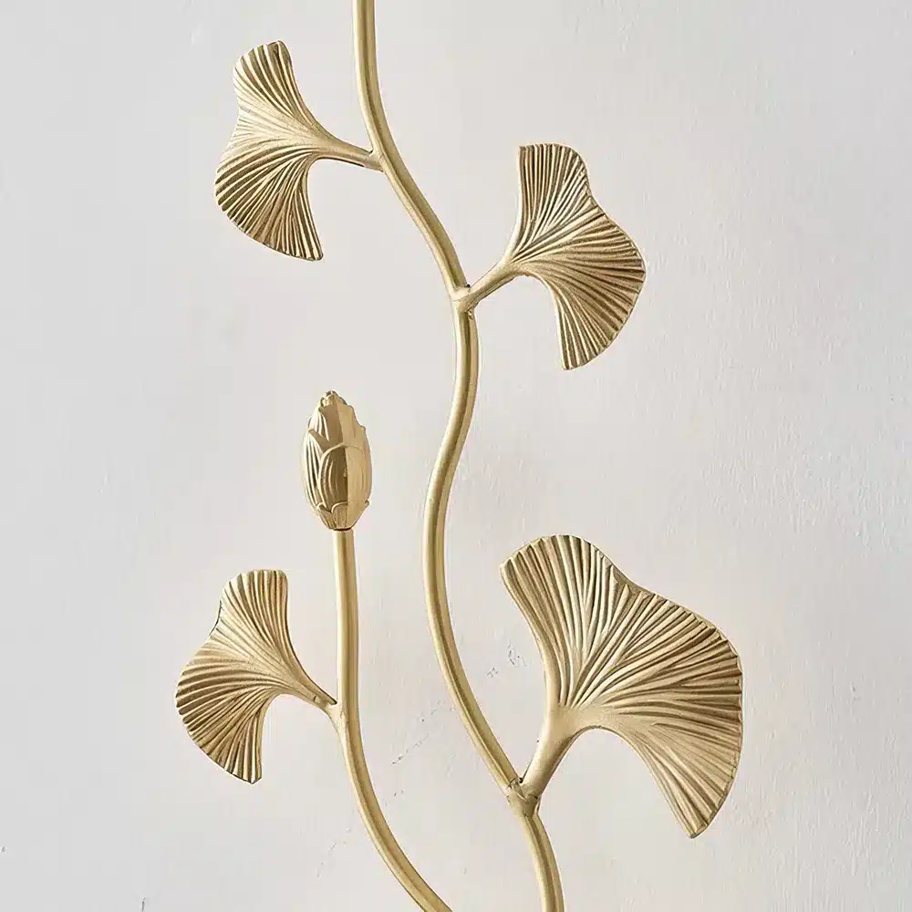 Gold metallic wall decor featuring stylized leaves and a central bud on curved stems, set against a plain white background.