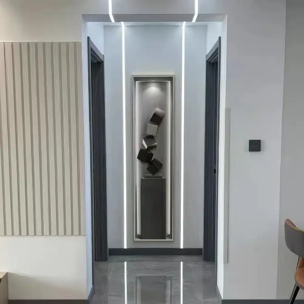 A modern hallway with sleek walls and ambient lighting. The floor is glossy, and the ceiling features a lit panel. A vertical art installation of stacked cubes is centered on the back wall between two doorways.