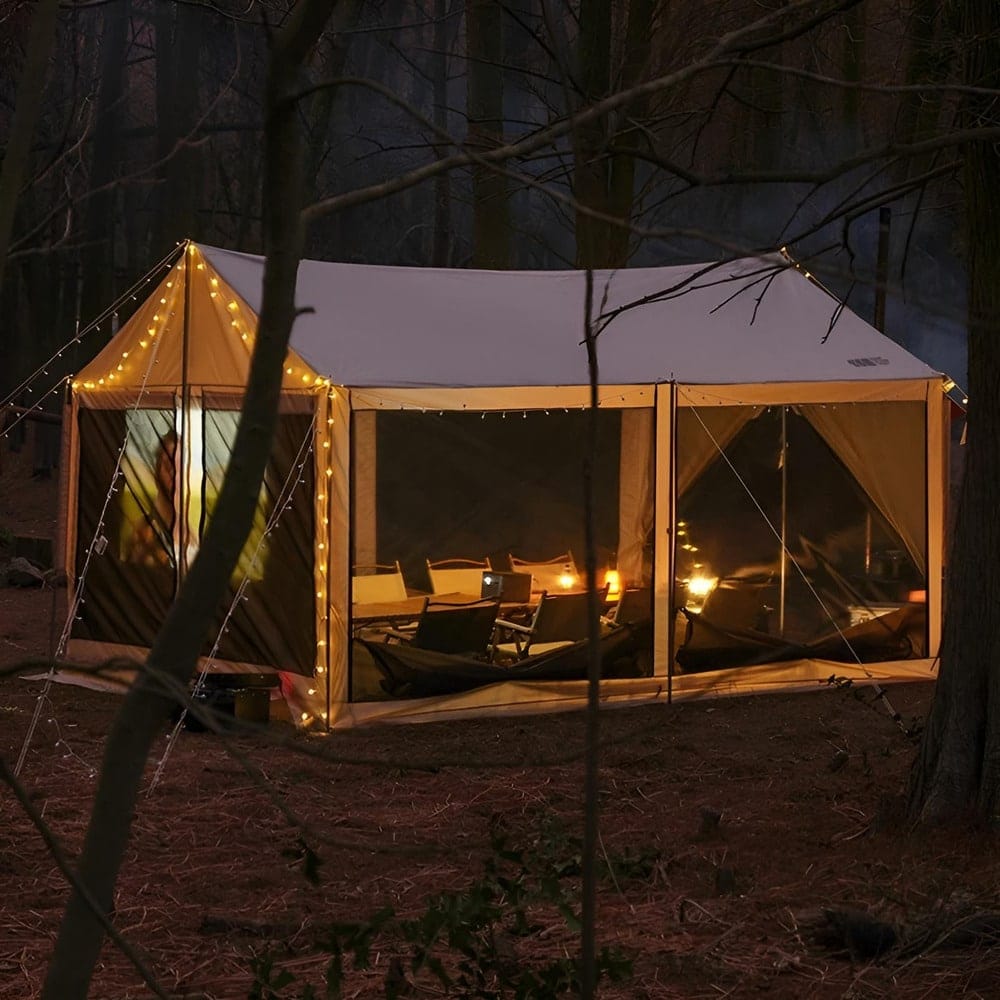 A well-lit tent in a forested area at dusk, surrounded by trees. The tent features a cozy interior with string lights along its edges and a warm glow from lanterns inside, creating an inviting atmosphere amid the darkening surroundings.