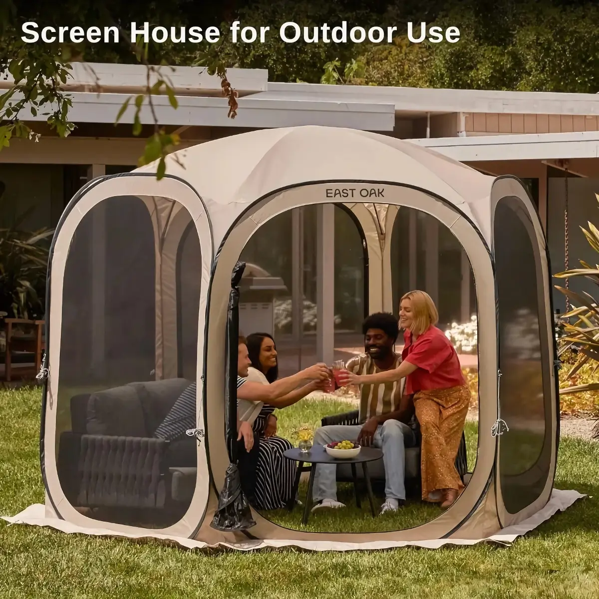 Four people sit inside a screened tent on a lawn, clinking glasses around a small table with snacks. The tent is positioned in front of a modern house. Text at the top reads, Screen House for Outdoor Use.